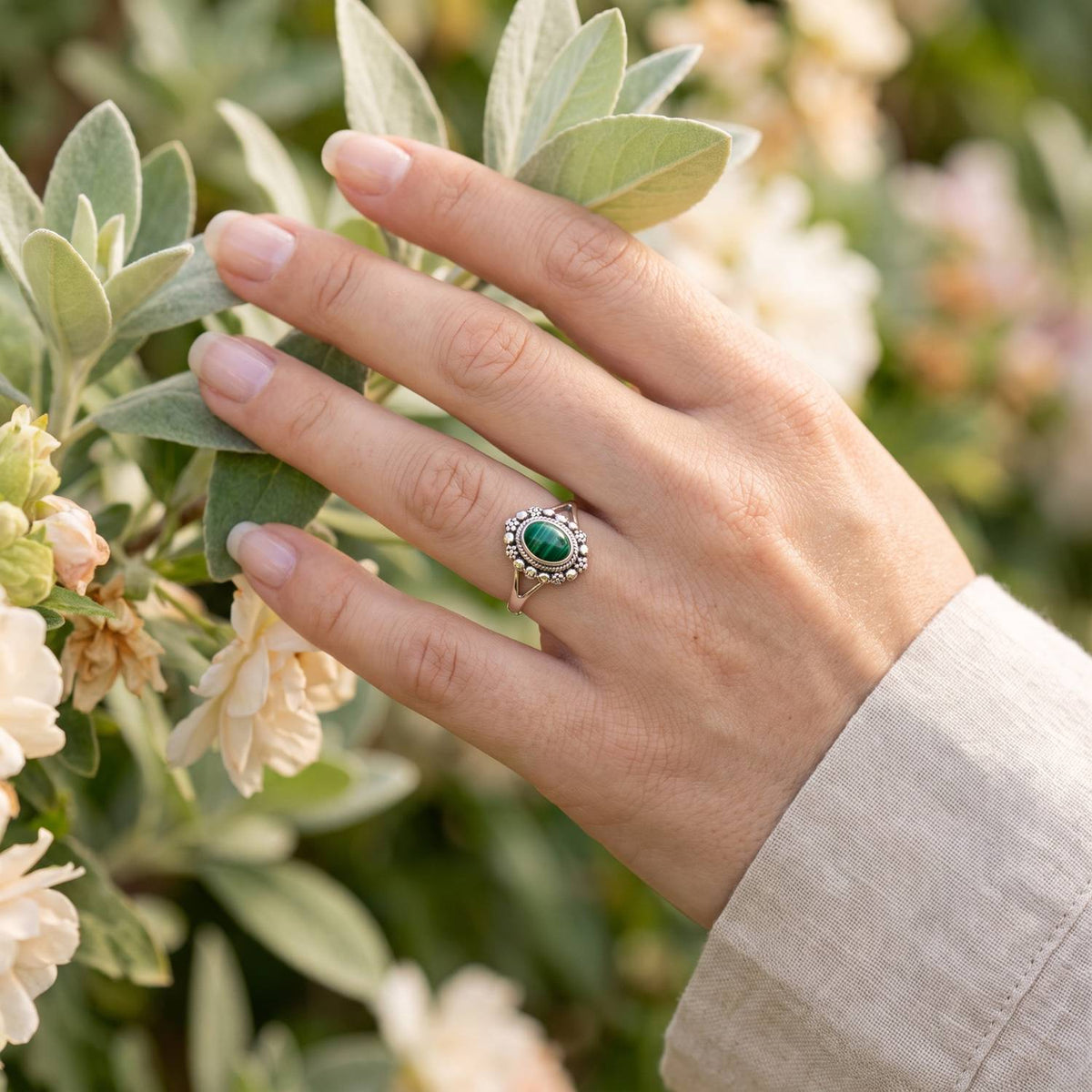 Silberring mit Malachit an der Hand zwischen Blumen