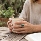 [KI] Malachitring aus Silber getragen beim Lesen mit einer Tasse