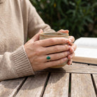 [KI] Malachitring aus Silber getragen beim Lesen mit einer Tasse