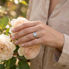 [KI] Silberring mit Mondstein an der Hand zwischen Blumen