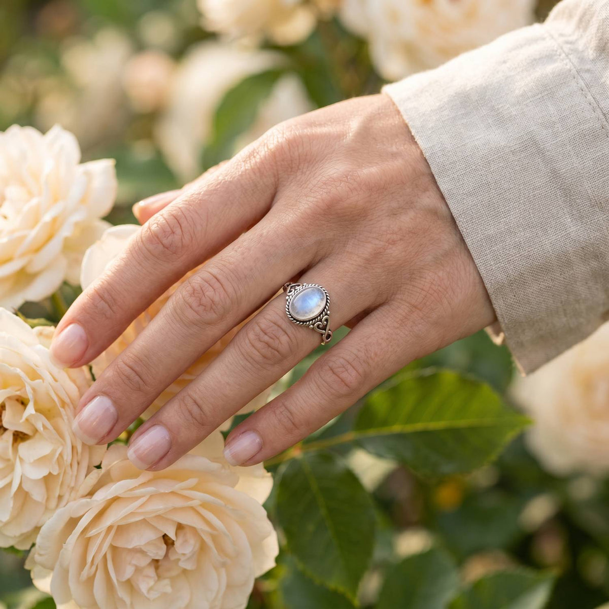 Silberring mit Mondstein an der Hand zwischen Blumen