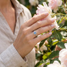 [KI] Silberring mit Mondstein an der Hand zwischen Blumen