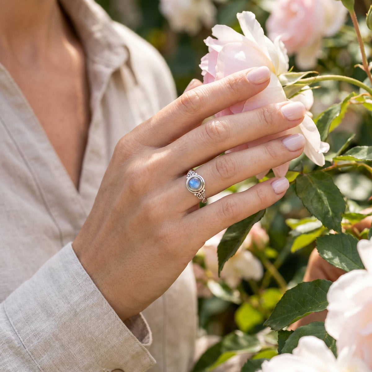 Silberring mit Mondstein an der Hand zwischen Blumen