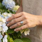 [KI] Silberring mit Mondstein an der Hand zwischen Blumen
