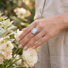 [KI] Silberring mit Mondstein an der Hand zwischen Blumen