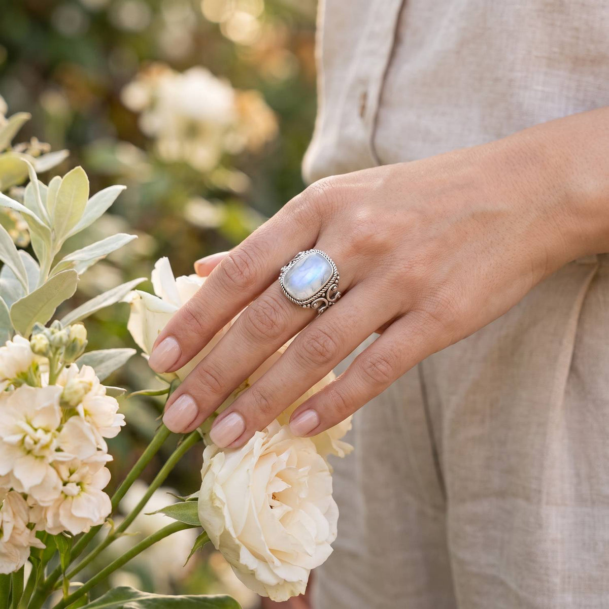 Silberring mit Mondstein an der Hand zwischen Blumen