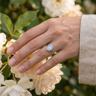 [KI] Silberring mit Mondstein an der Hand zwischen Blumen