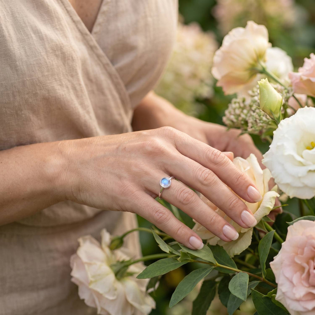 Silberring mit Mondstein an der Hand zwischen Blumen