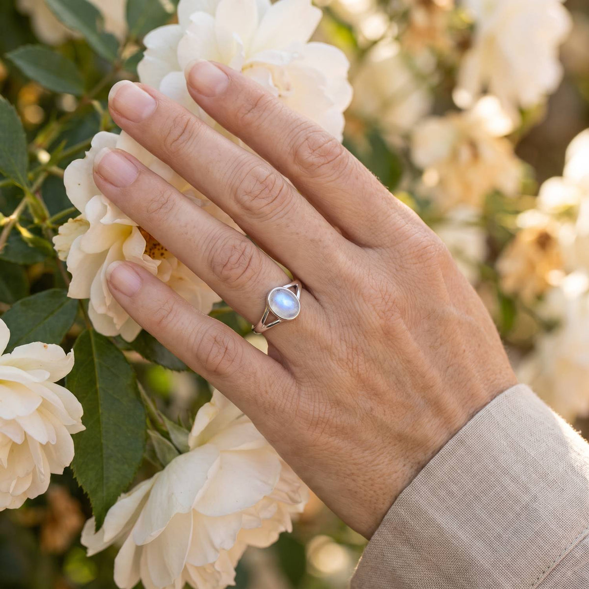 Silberring mit Mondstein an der Hand zwischen Blumen