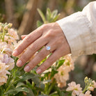 [KI] Silberring mit Mondstein an der Hand zwischen Blumen
