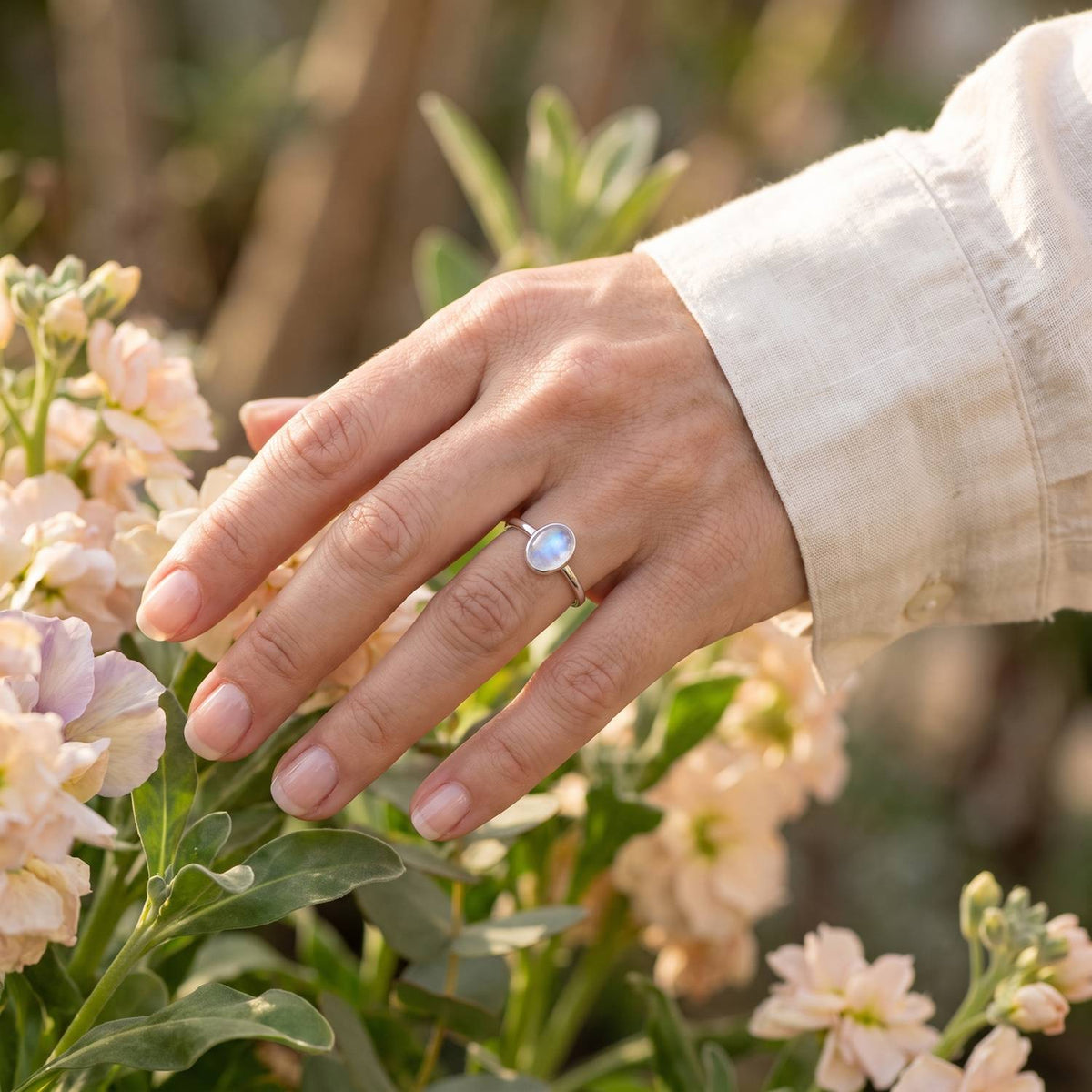 Silberring mit Mondstein an der Hand zwischen Blumen