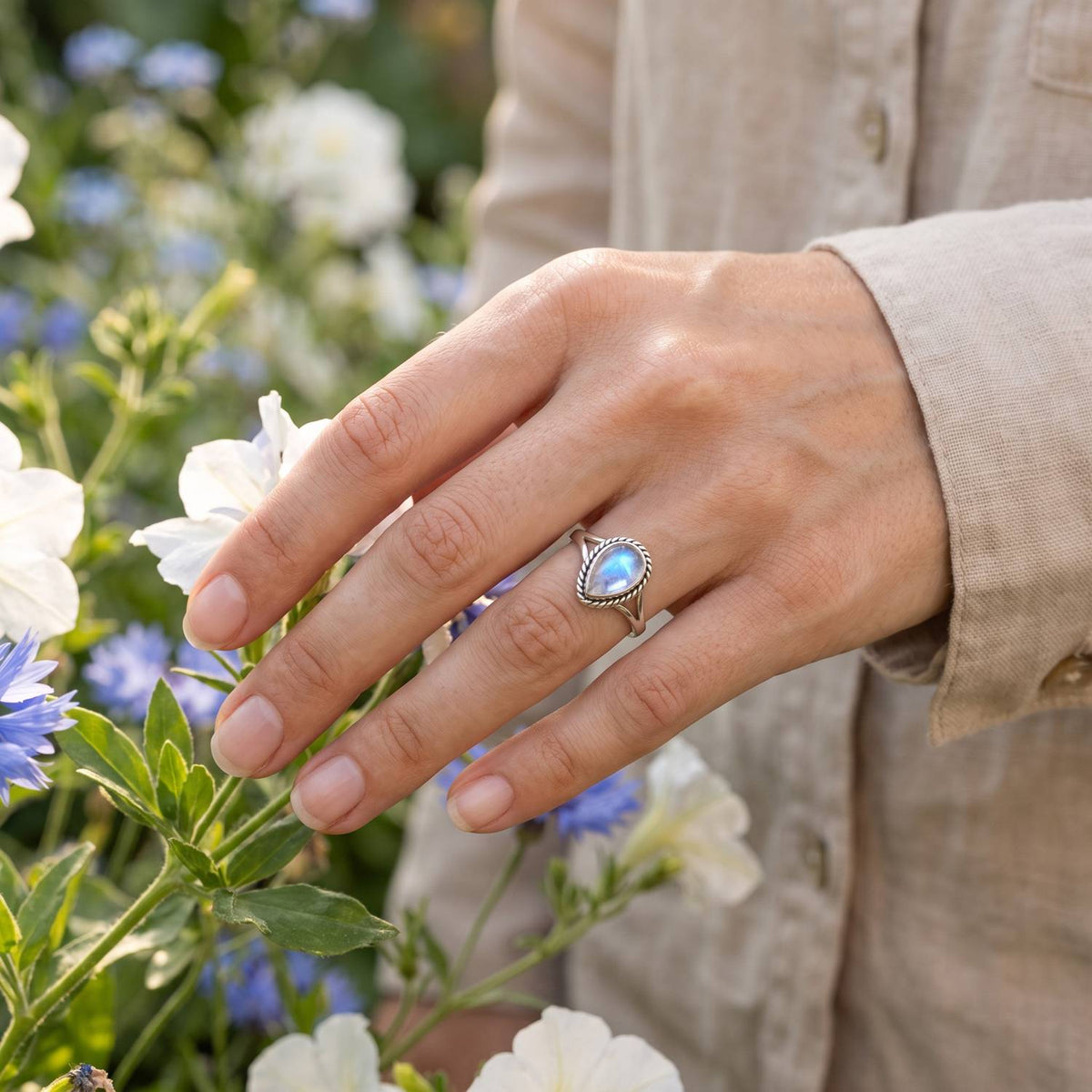 Silberring mit Mondstein an der Hand zwischen Blumen