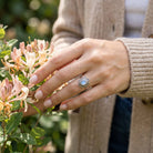 [KI] Silberring mit Mondstein an der Hand zwischen Blumen