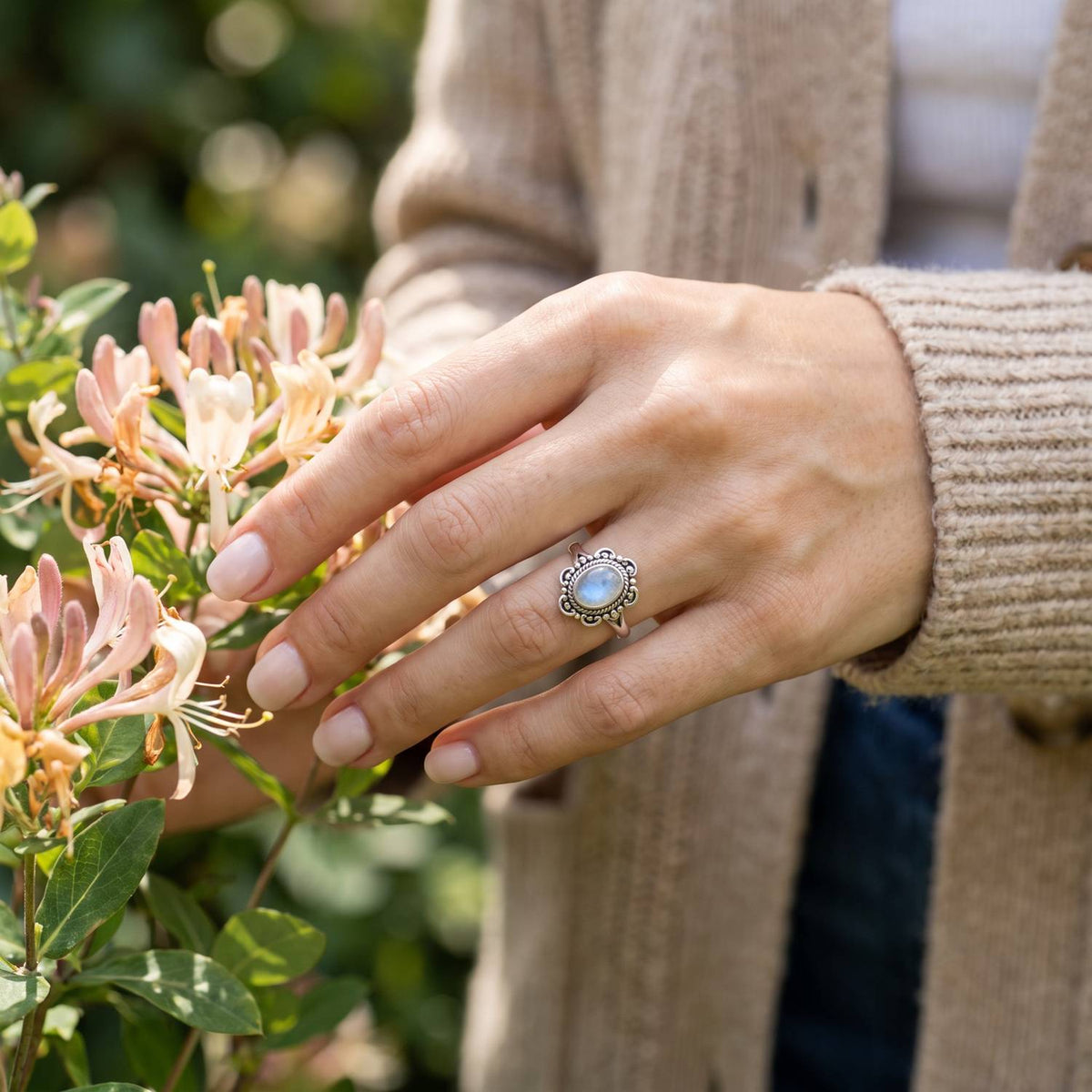 Silberring mit Mondstein an der Hand zwischen Blumen