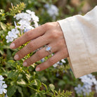 [KI] Silberring mit Mondstein an der Hand zwischen Blumen