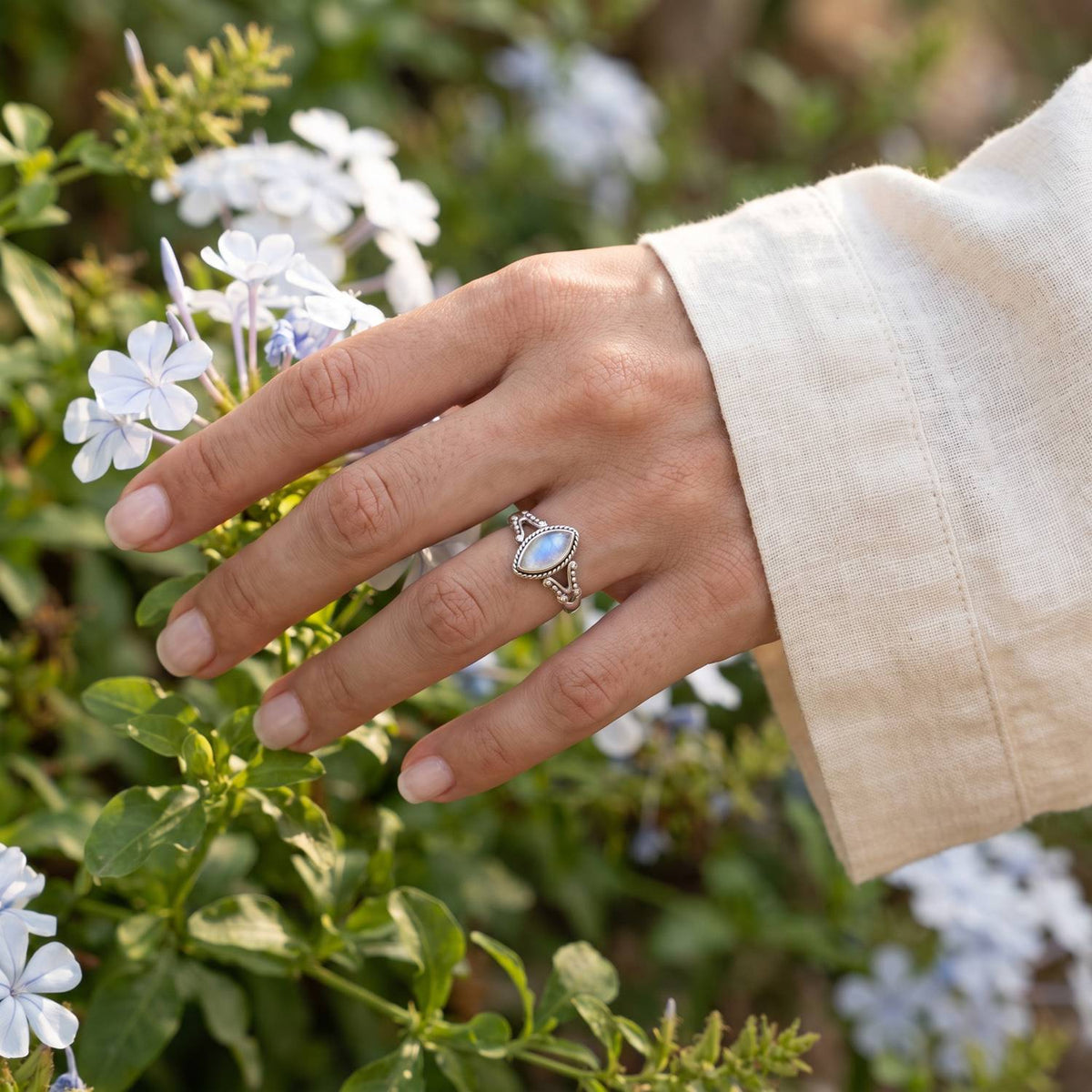 Silberring mit Mondstein an der Hand zwischen Blumen