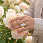 [KI] Silberring mit Mondstein an der Hand zwischen Blumen