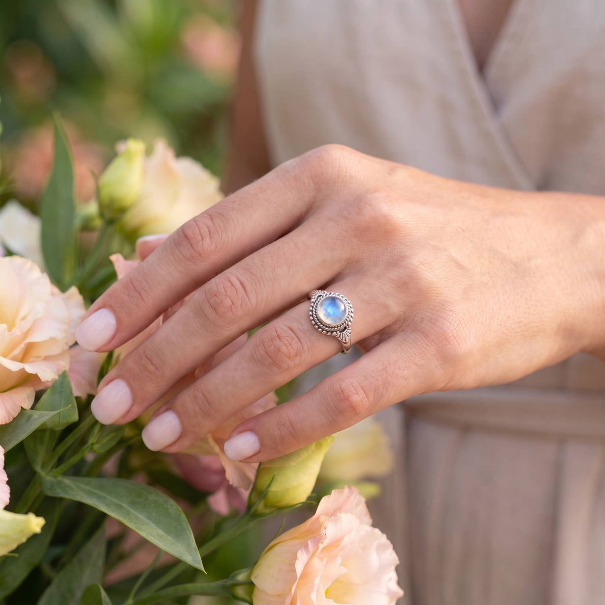 Silberring mit Mondstein an der Hand zwischen Blumen