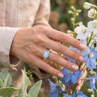 [KI] Silberring mit Mondstein an der Hand zwischen Blumen