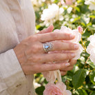 [KI] Silberring mit Mondstein an der Hand zwischen Blumen