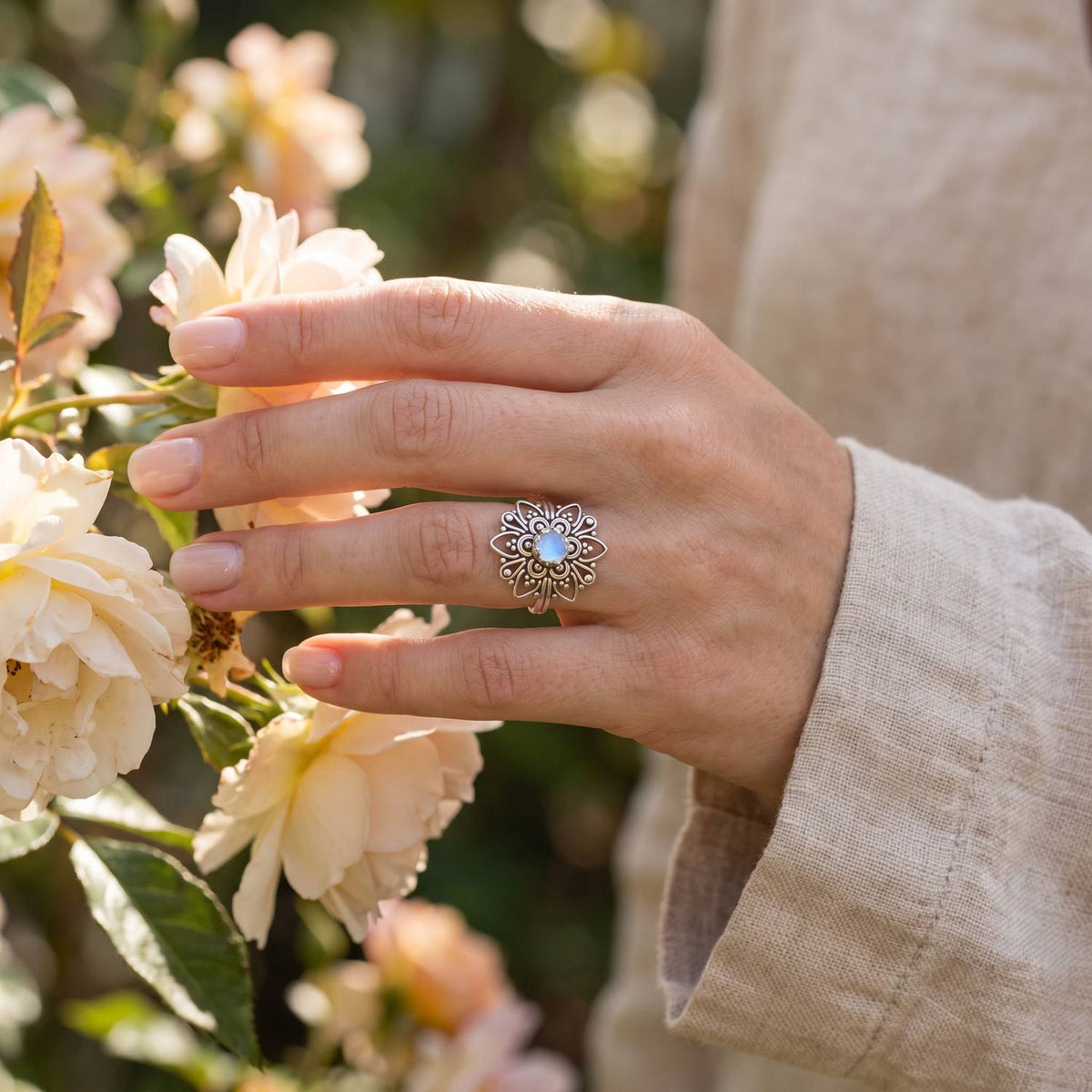 Silberring mit Mondstein an der Hand zwischen Blumen