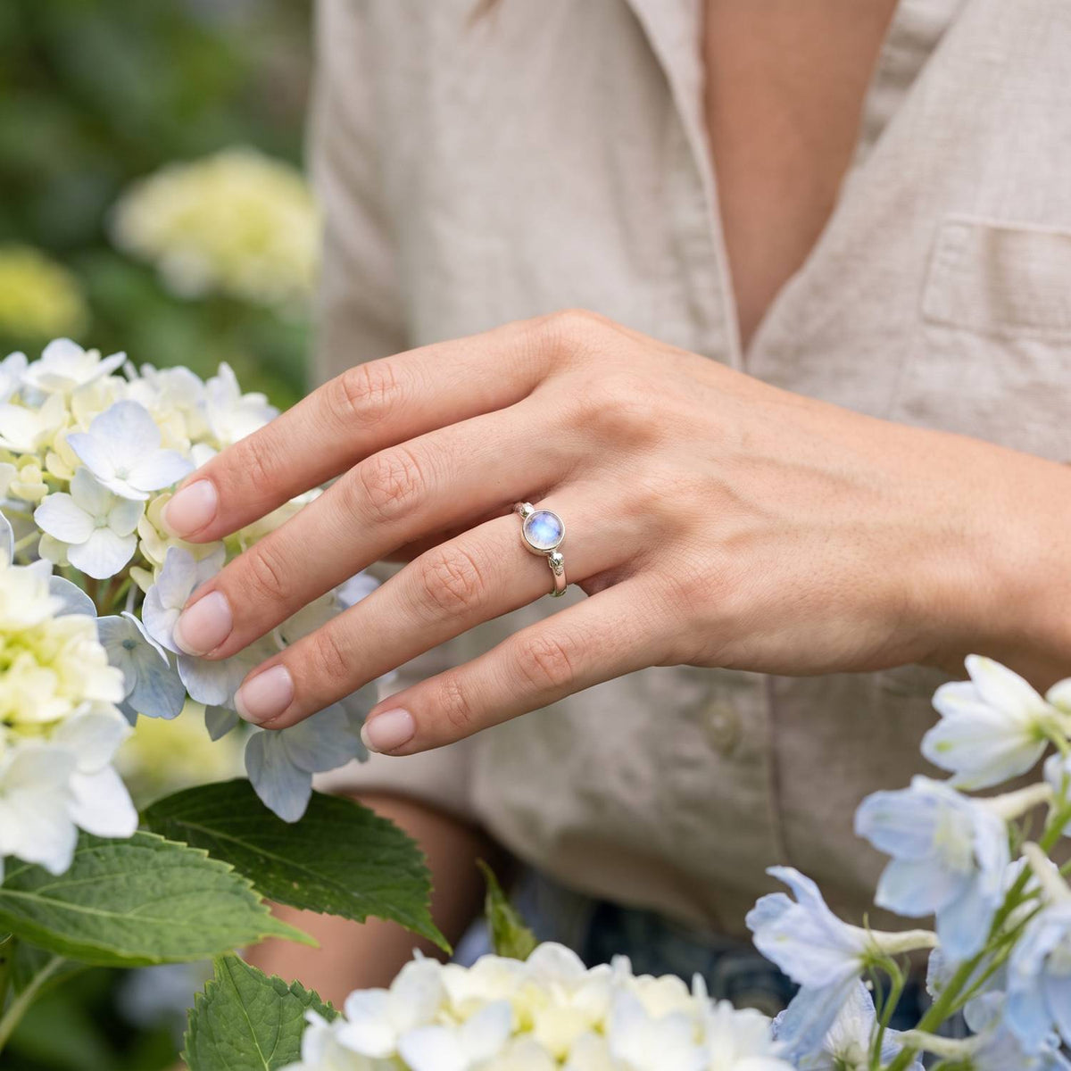 Silberring mit Mondstein an der Hand zwischen Blumen