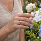 [KI] Silberring mit Mondstein an der Hand zwischen Blumen