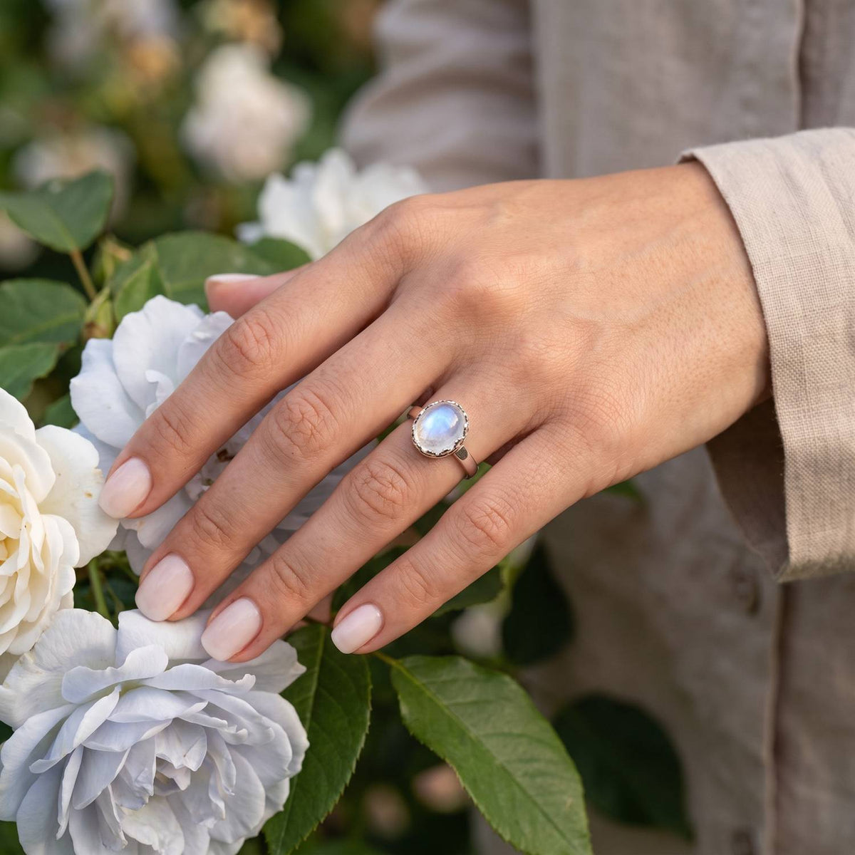 Silberring mit Mondstein an der Hand zwischen Blumen