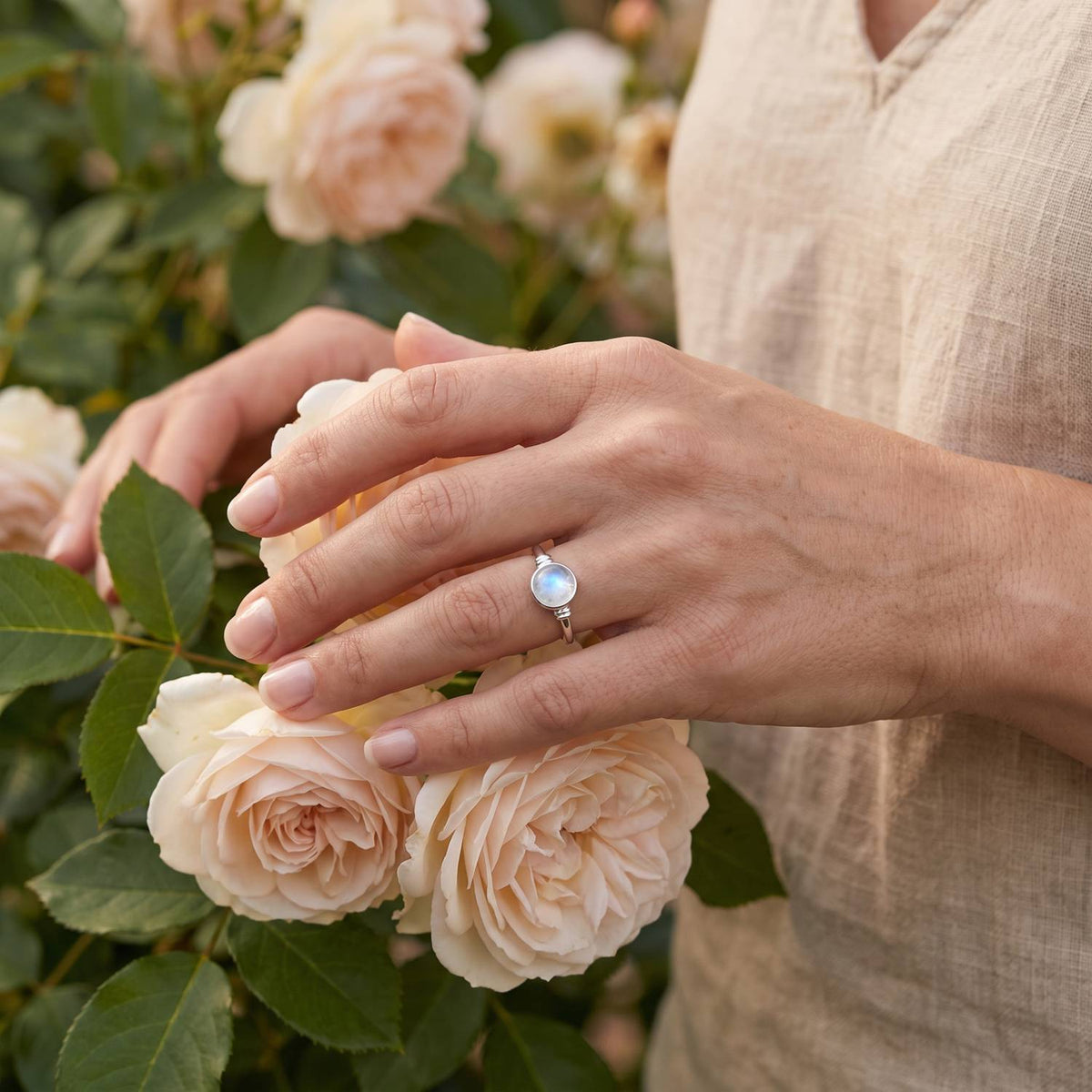 Silberring mit Mondstein an der Hand zwischen Blumen