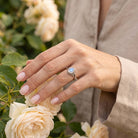 [KI] Silberring mit Mondstein an der Hand zwischen Blumen