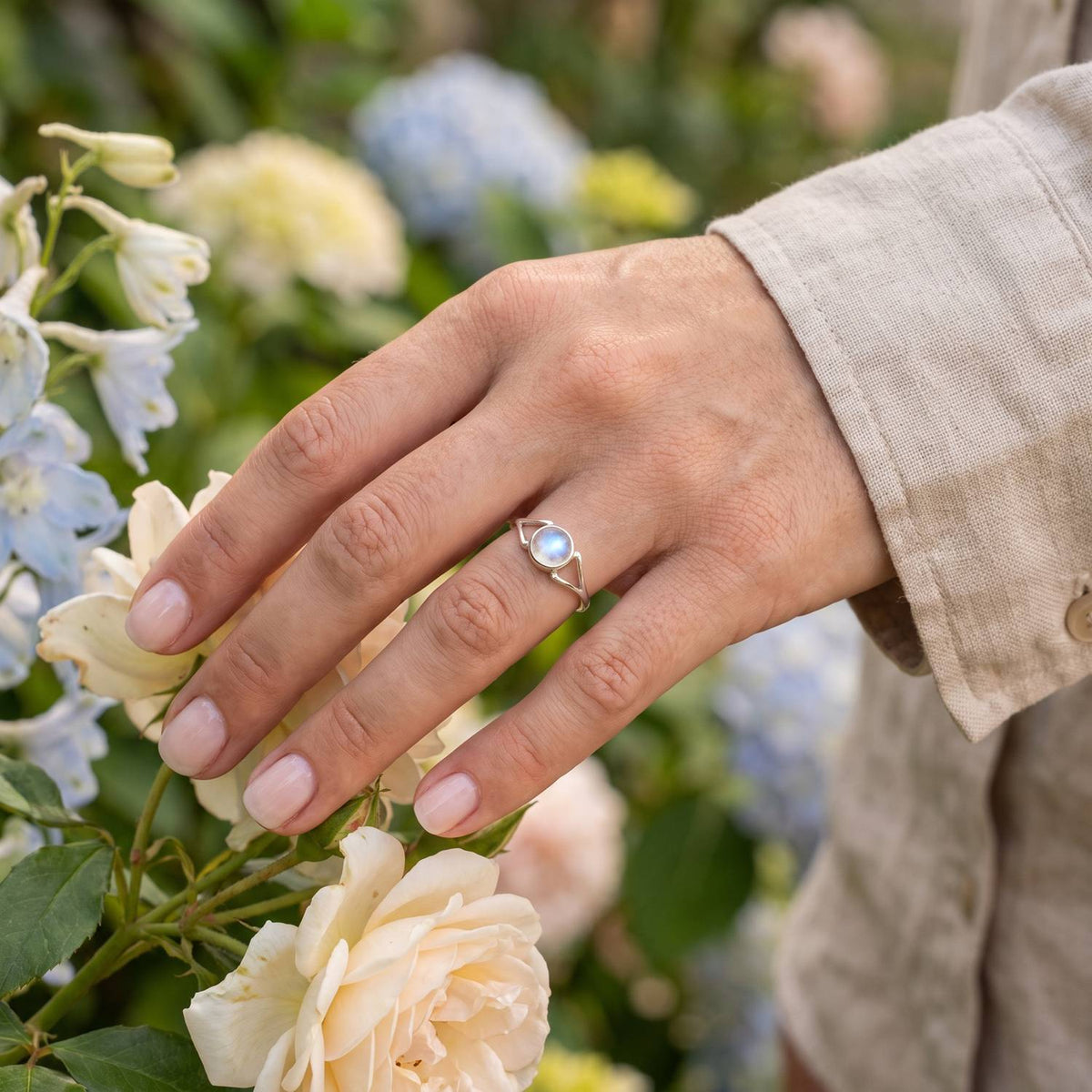 Silberring mit Mondstein an der Hand zwischen Blumen