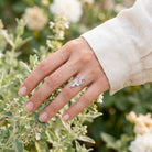 [KI] Silberring mit Mondstein an der Hand zwischen Blumen