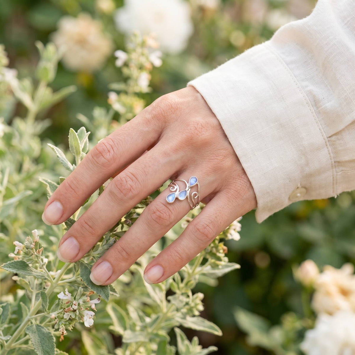 Silberring mit Mondstein an der Hand zwischen Blumen