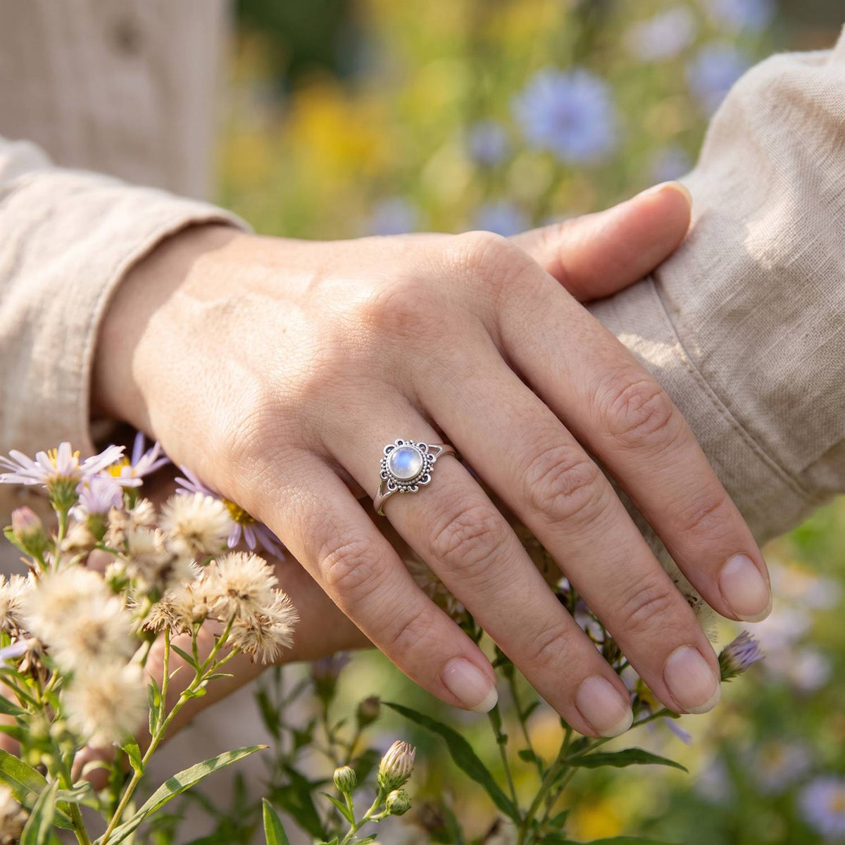 Silberring mit Mondstein an der Hand zwischen Blumen