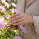 [KI] Silberring mit Mondstein an der Hand zwischen Blumen
