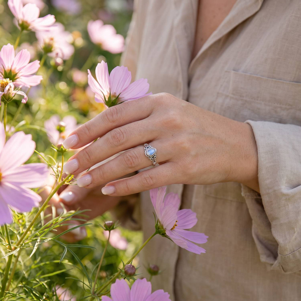 Silberring mit Mondstein an der Hand zwischen Blumen