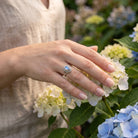 [KI] Silberring mit Mondstein an der Hand zwischen Blumen