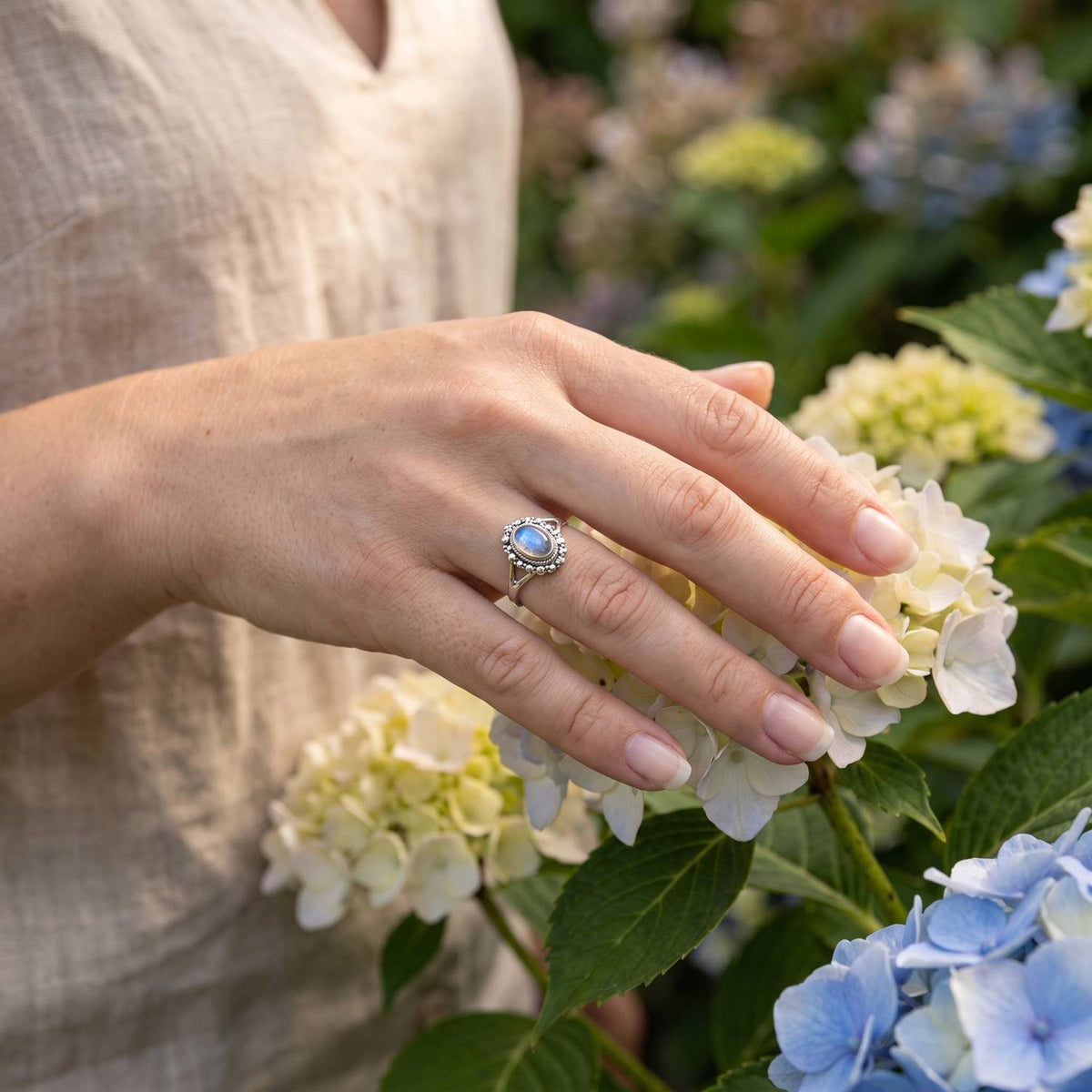 Silberring mit Mondstein an der Hand zwischen Blumen