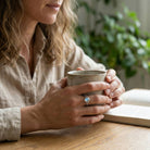 [KI] Mondsteinring aus Silber getragen beim Lesen mit einer Tasse