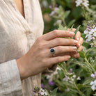 [KI] Silberring mit Onyx an der Hand zwischen Blumen