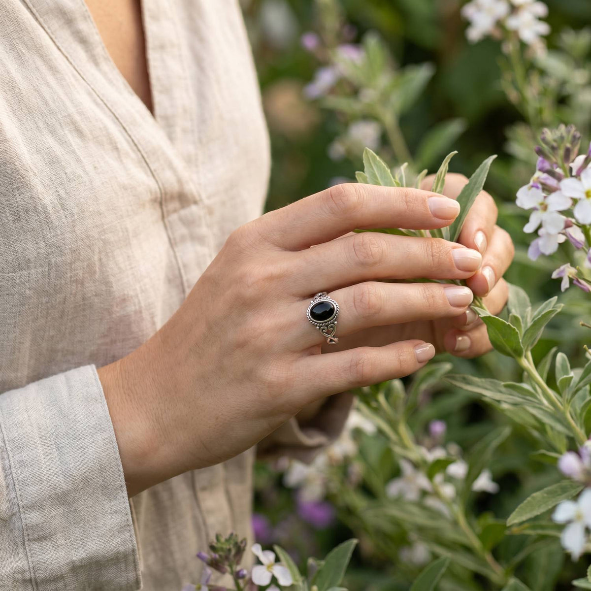 Silberring mit Onyx an der Hand zwischen Blumen
