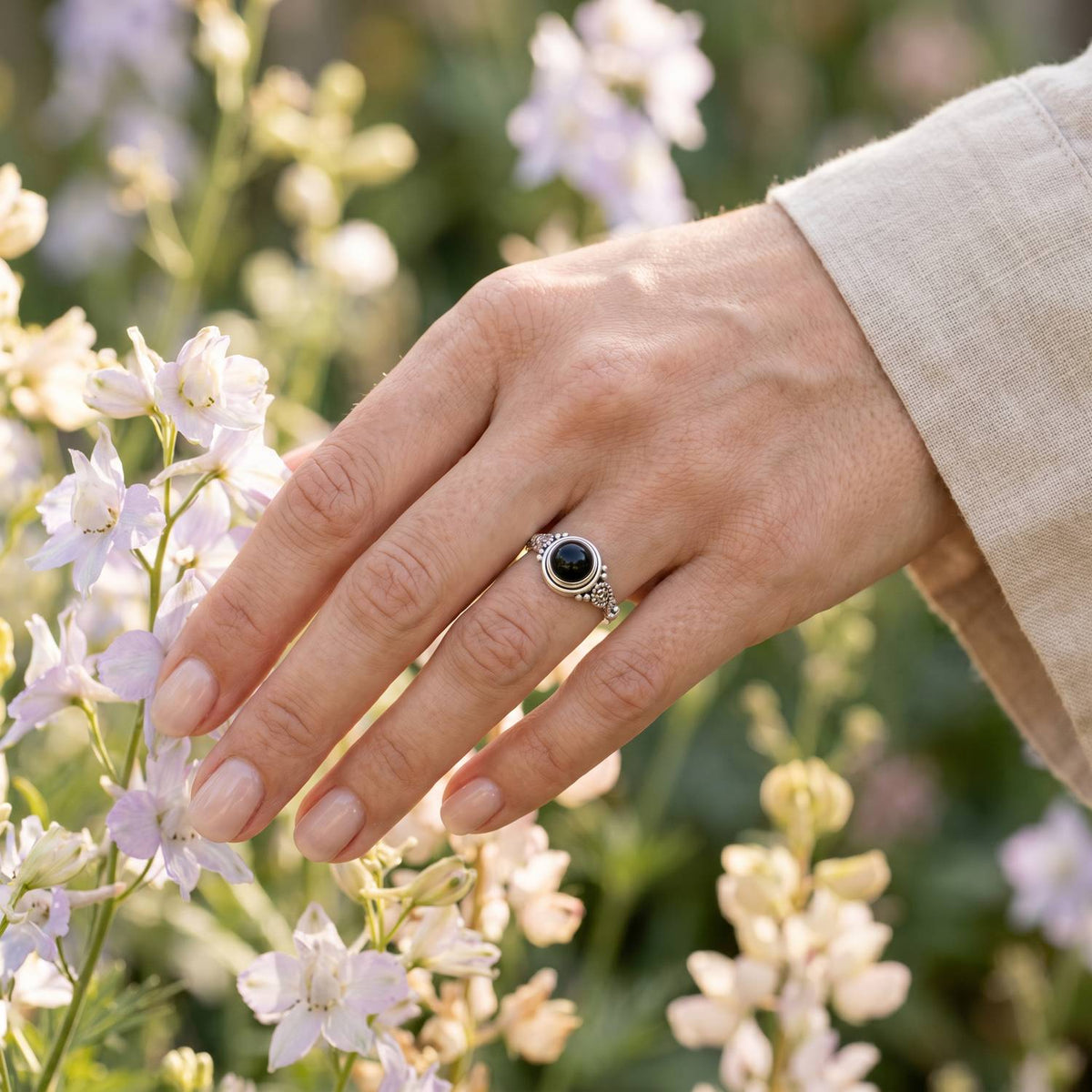 Silberring mit Onyx an der Hand zwischen Blumen