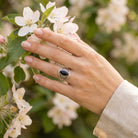 [KI] Silberring mit Onyx an der Hand zwischen Blumen