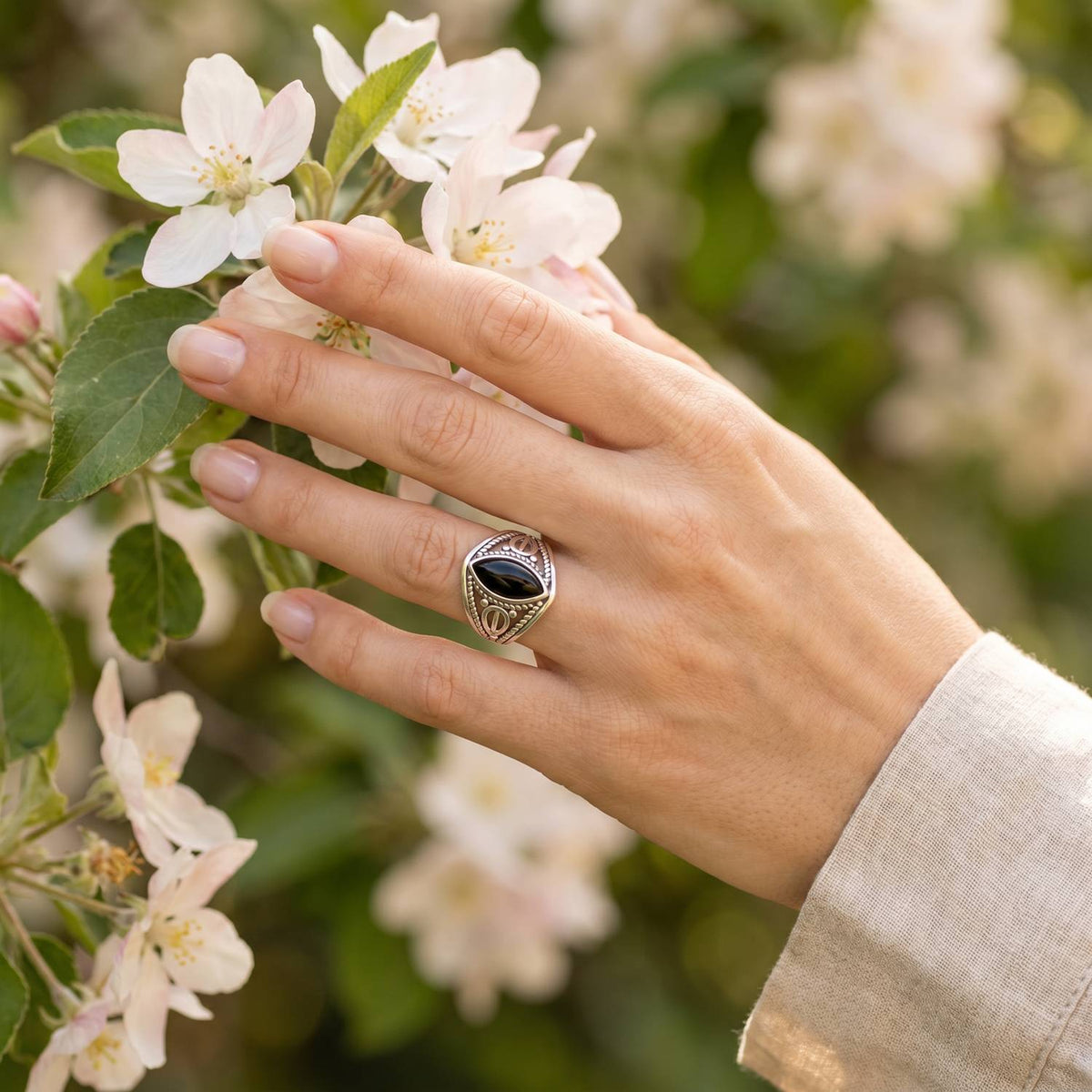 Silberring mit Onyx an der Hand zwischen Blumen