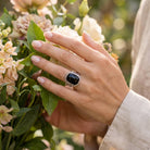 [KI] Silberring mit Onyx an der Hand zwischen Blumen