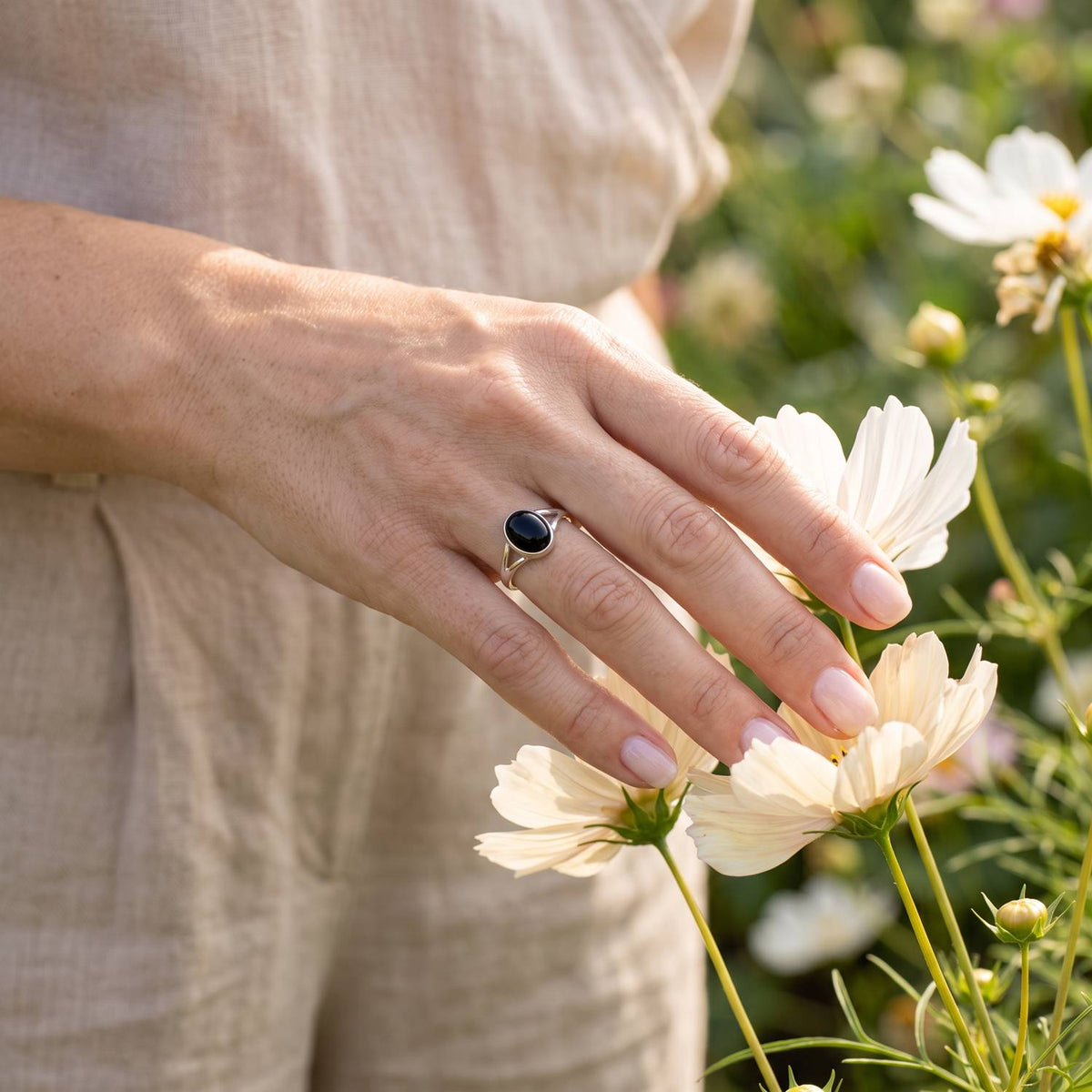 Silberring mit Onyx an der Hand zwischen Blumen
