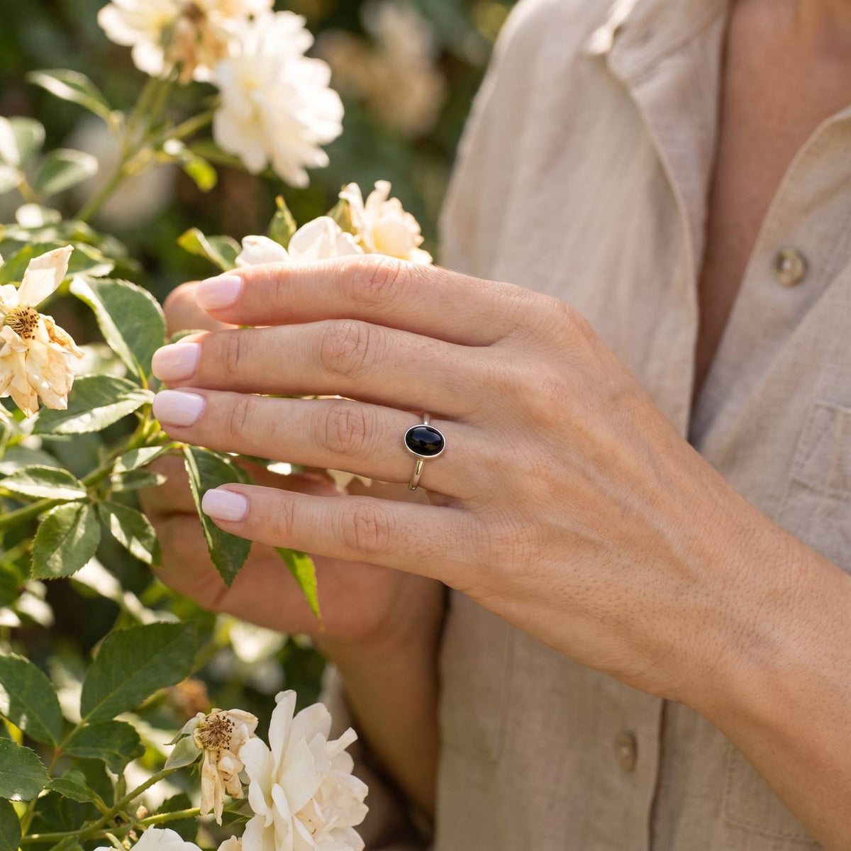 Silberring mit Onyx an der Hand zwischen Blumen