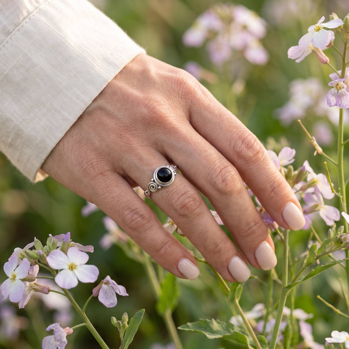 Silberring mit Onyx an der Hand zwischen Blumen