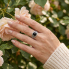 [KI] Silberring mit Onyx an der Hand zwischen Blumen