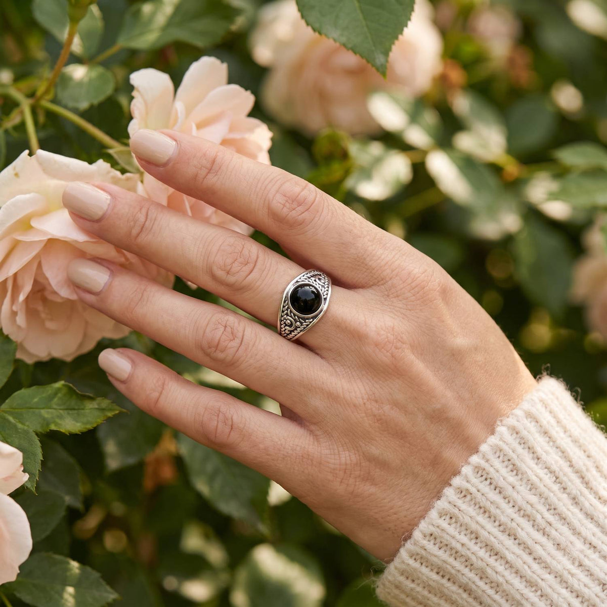 Silberring mit Onyx an der Hand zwischen Blumen